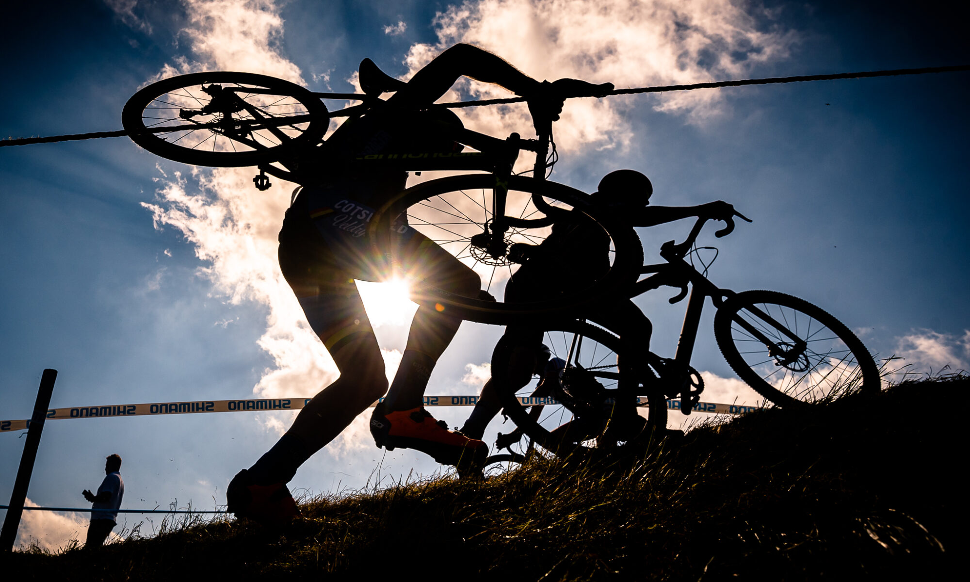 Silhouette of CX racer carrying bike up bank